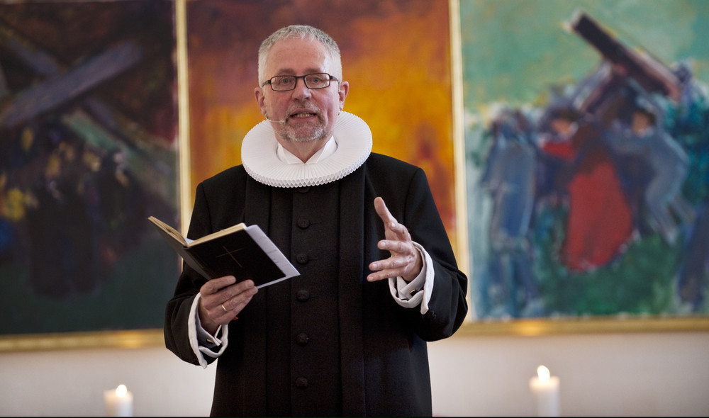Præst står i præstekjole foran alter med Ritualbog i hånden og taler